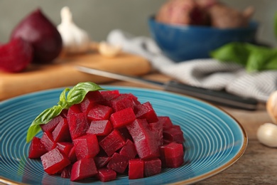 Photo of Plate of cut boiled beets with basil on wooden table, closeup