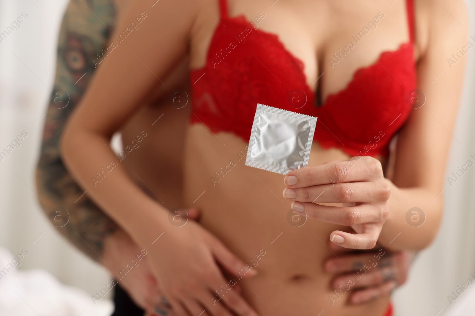 Photo of Young couple holding condom indoors, closeup view