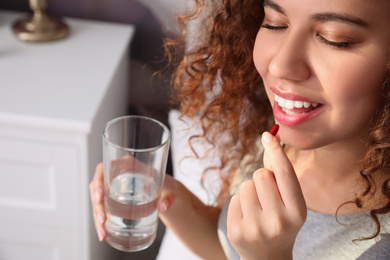 African-American woman with glass of water taking vitamin pill at home, closeup