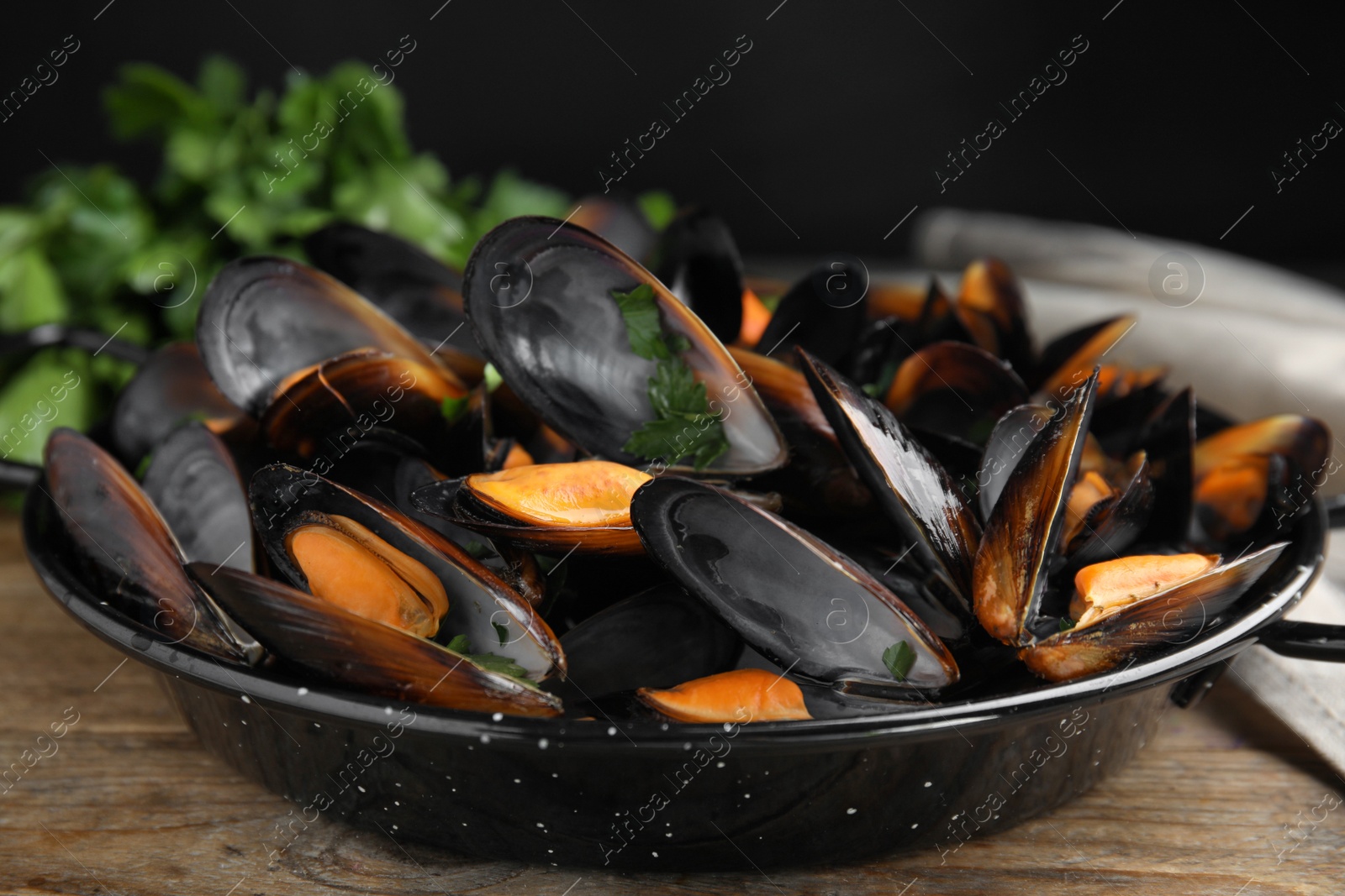Photo of Pan of cooked mussels with parsley on wooden table, closeup