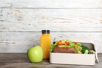 Healthy food for school child in lunch box on table against wooden wall