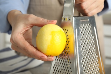 Woman zesting fresh lemon indoors, closeup view