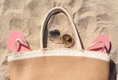 Pink flip flops, sunglasses and straw bag on sand, flat lay. Beach accessories