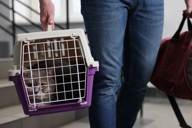 Travel with pet. Man holding carrier with cute cat and bag indoors, closeup