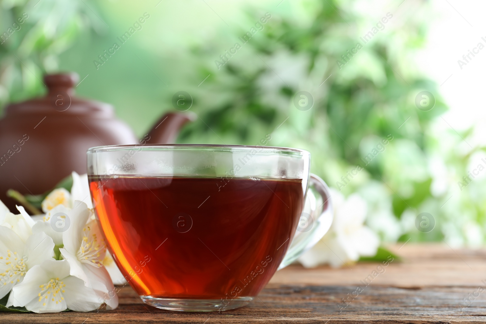 Photo of Cup of tea and fresh jasmine flowers on wooden table. Space for text