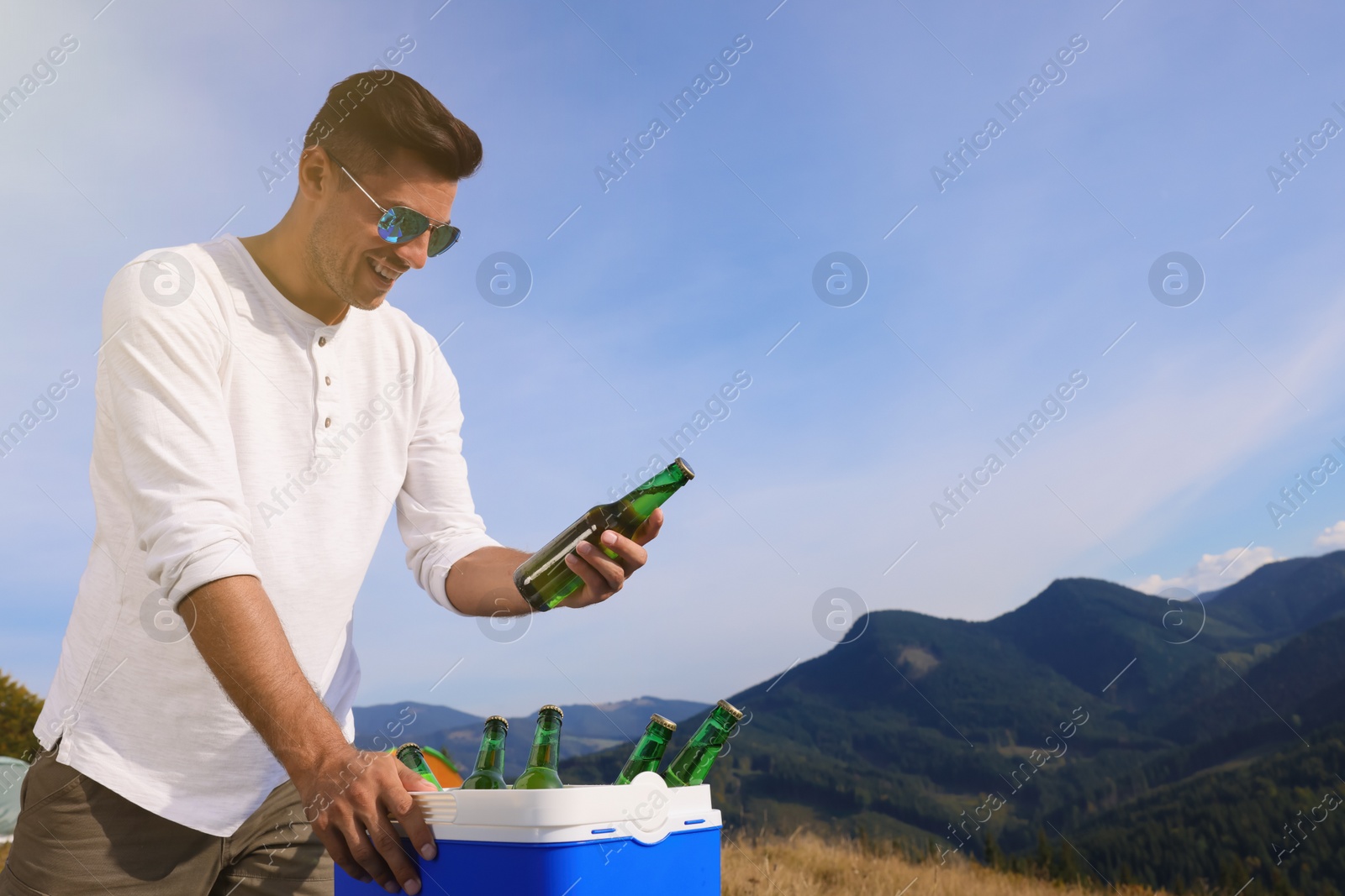 Photo of Man taking bottle of beer from cool box in mountains. Space for text