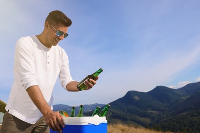 Man taking bottle of beer from cool box in mountains. Space for text