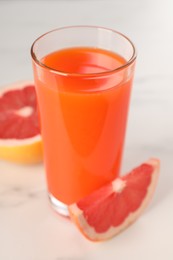 Tasty grapefruit juice in glass and fresh fruit on white table, closeup