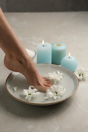 Photo of Woman soaking her foot in bowl with water and flowers on grey marble floor, closeup. Pedicure procedure