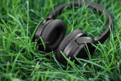 Photo of Black wireless headphones on green grass outdoors, closeup