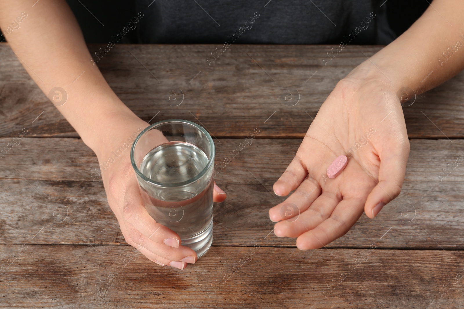 Photo of Woman holding pill and glass of water at table, closeup