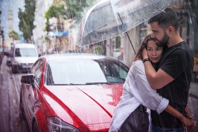 Young couple with umbrella enjoying time together under rain on city street