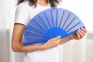 Photo of Woman with blue hand fan indoors, closeup