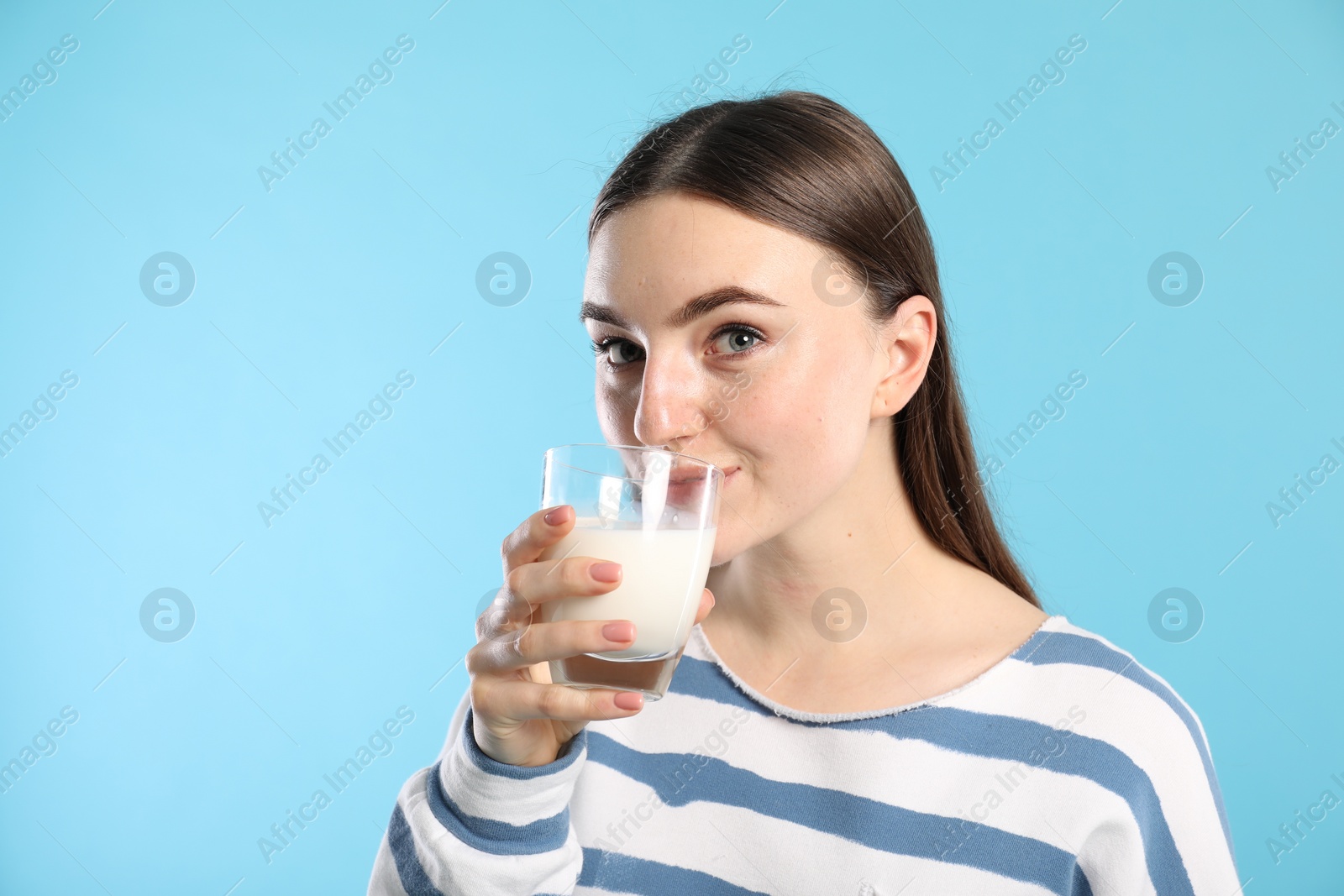 Photo of Beautiful woman drinking milk on light blue background, space for text