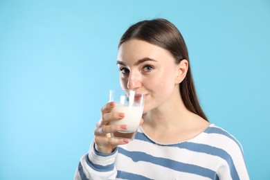 Beautiful woman drinking milk on light blue background, space for text