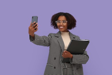 Photo of African American intern with folders taking selfie on purple background