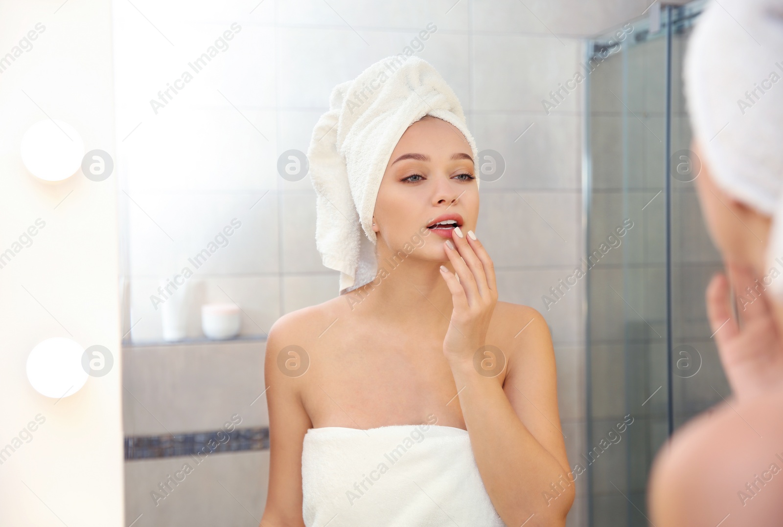 Photo of Beautiful woman with clean towels near mirror in bathroom