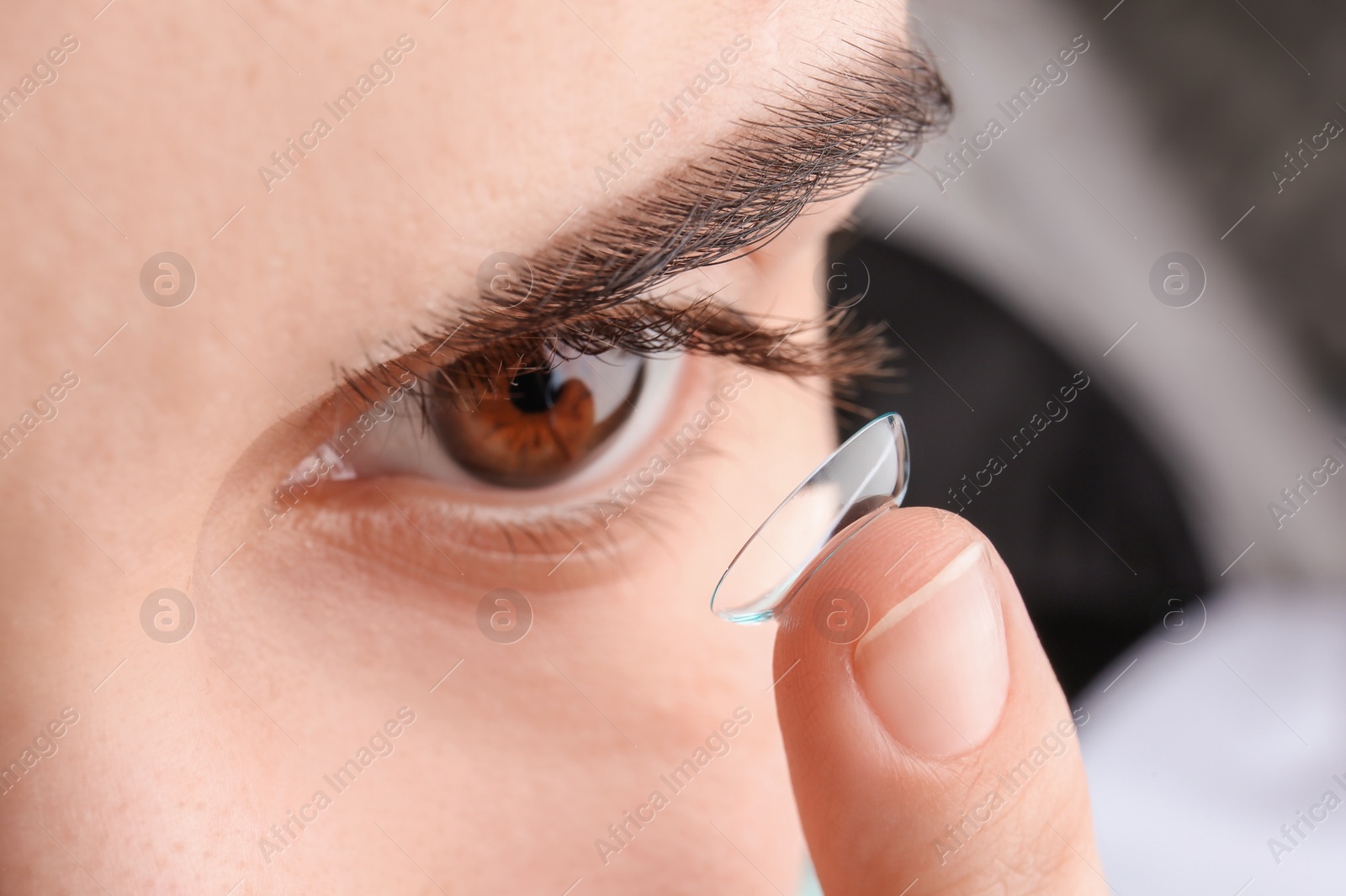 Photo of Young woman putting contact lens in her eye, closeup