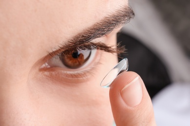 Photo of Young woman putting contact lens in her eye, closeup