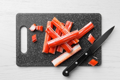 Photo of Delicious crab sticks with knife on white wooden table, top view