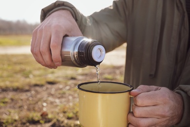 Photo of Man pouring hot drink into mug from thermos outdoors, closeup