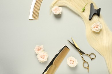 Flat lay composition with professional hairdresser tools, flowers and blonde hair strand on light grey background. Space for text