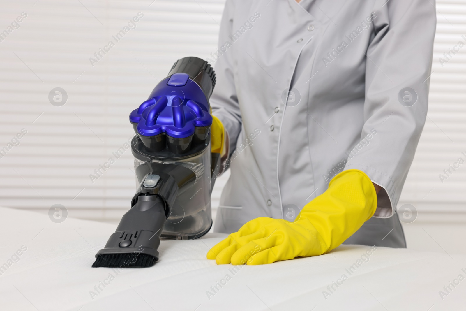 Photo of Woman in gloves disinfecting mattress with vacuum cleaner indoors, closeup