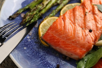 Photo of Tasty grilled salmon with asparagus, lemon and spices served on table, closeup