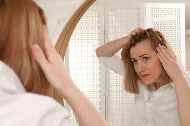 Emotional woman suffering from baldness near mirror at home