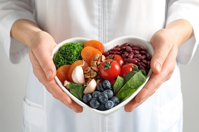 Photo of Doctor holding bowl with products for heart-healthy diet, closeup