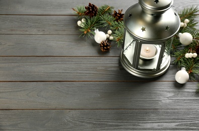 Photo of Christmas lantern with burning candle and festive decor on grey wooden table. Space for text