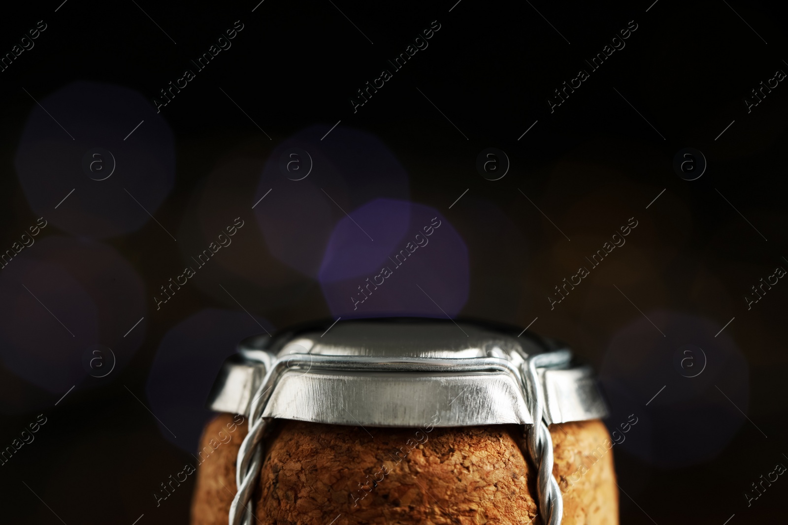 Photo of Sparkling wine cork with muselet cap against blurred festive lights, closeup. Space for text