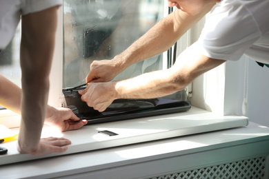 Photo of Professional workers tinting window with foil indoors, closeup