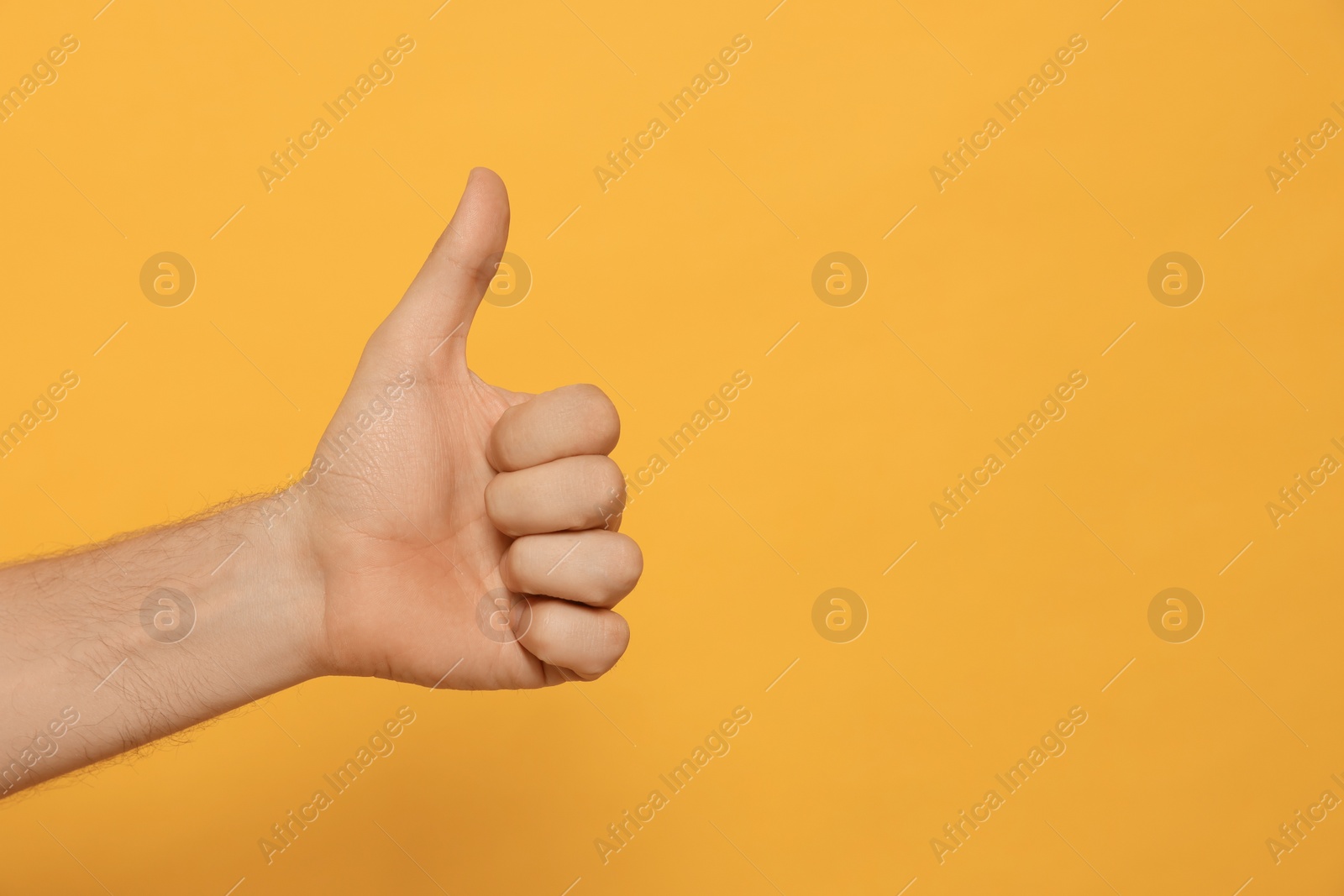 Photo of Man showing thumb up on orange background, closeup. Space for text