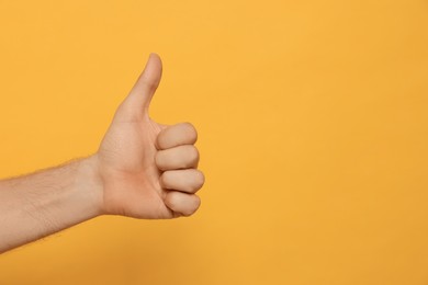 Photo of Man showing thumb up on orange background, closeup. Space for text
