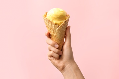 Photo of Woman holding waffle cone with delicious yellow ice cream on pink background, closeup