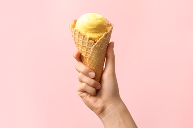 Woman holding waffle cone with delicious yellow ice cream on pink background, closeup