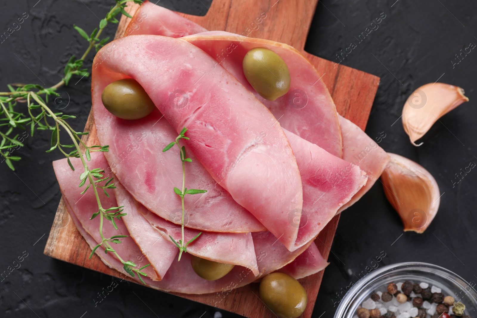 Photo of Tasty ham with olives, garlic and thyme on black textured table, flat lay