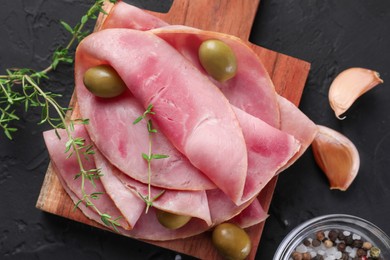 Photo of Tasty ham with olives, garlic and thyme on black textured table, flat lay