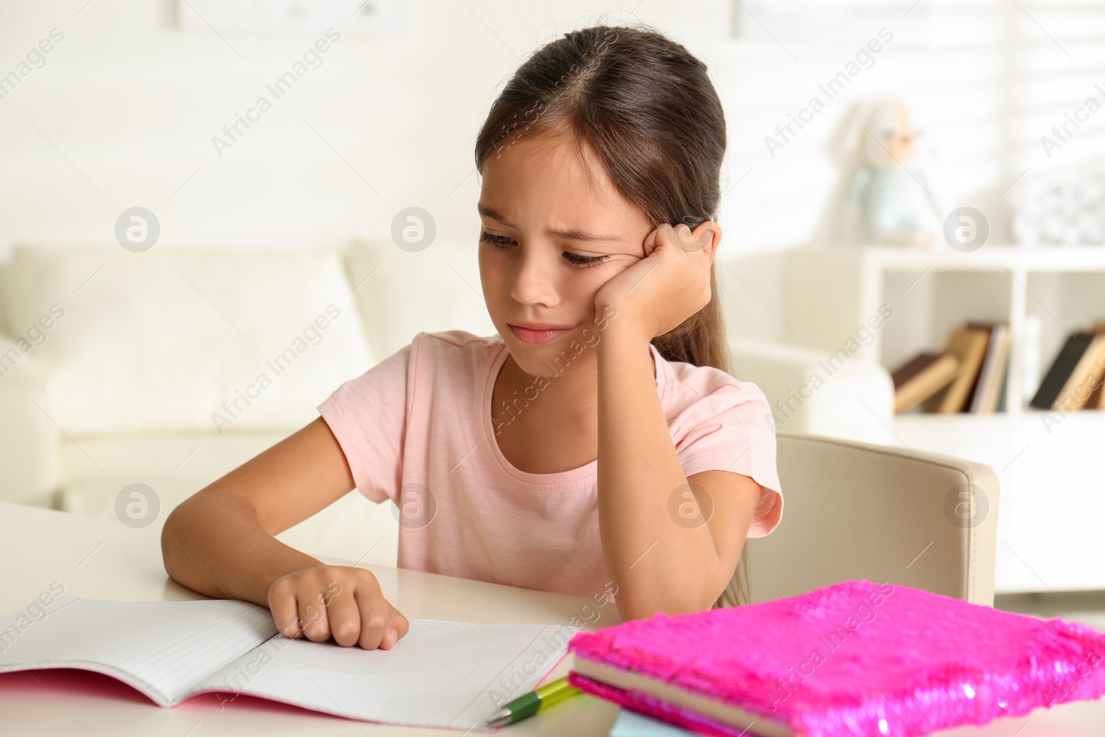 Photo of Sad little girl doing homework at table indoors