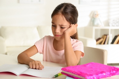 Sad little girl doing homework at table indoors