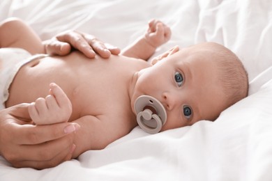 Photo of Mother and her cute little baby with pacifier on bed, closeup