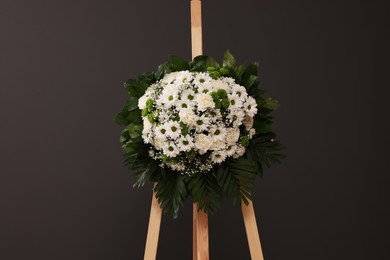 Photo of Funeral wreath of flowers on wooden stand against grey background