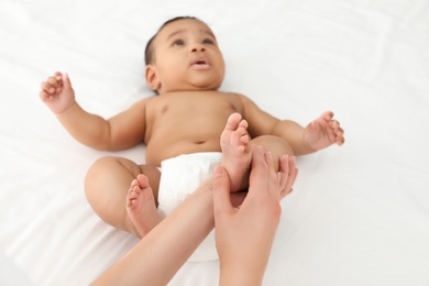 Photo of Mother and her cute child on white bed, closeup. Baby massage and exercises