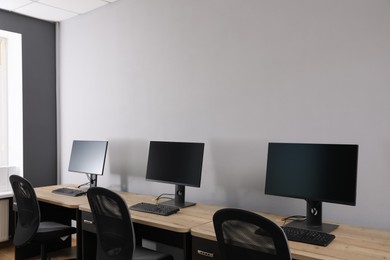 Photo of Open office interior. Modern workplaces with computers near light grey wall