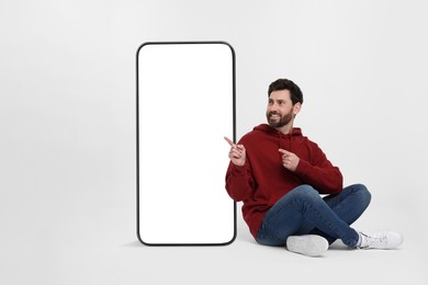 Image of Man pointing at huge mobile phone with empty screen on grey background. Mockup for design