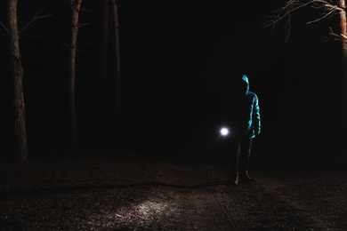 Man with bright flashlight in forest at night