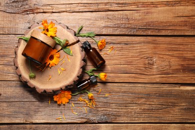 Different cosmetic products and beautiful calendula flowers on wooden table, flat lay. Space for text