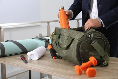 Photo of Businessman packing sports stuff for training into bag in office, closeup