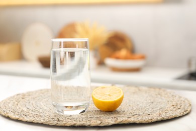 Photo of Glass with clear water and half of lemon on table in kitchen